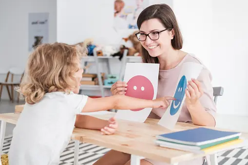 Una mujer y una niña trabajan con tarjetas que representan distintas expresiones emocionales.