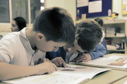 Dos alumnos leyendo y trabajando con libros en el aula.