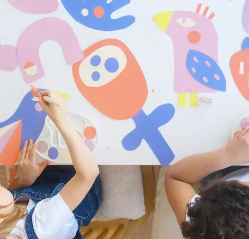 Niños realizando juntos una actividad artística con pintura y figuras de colores.