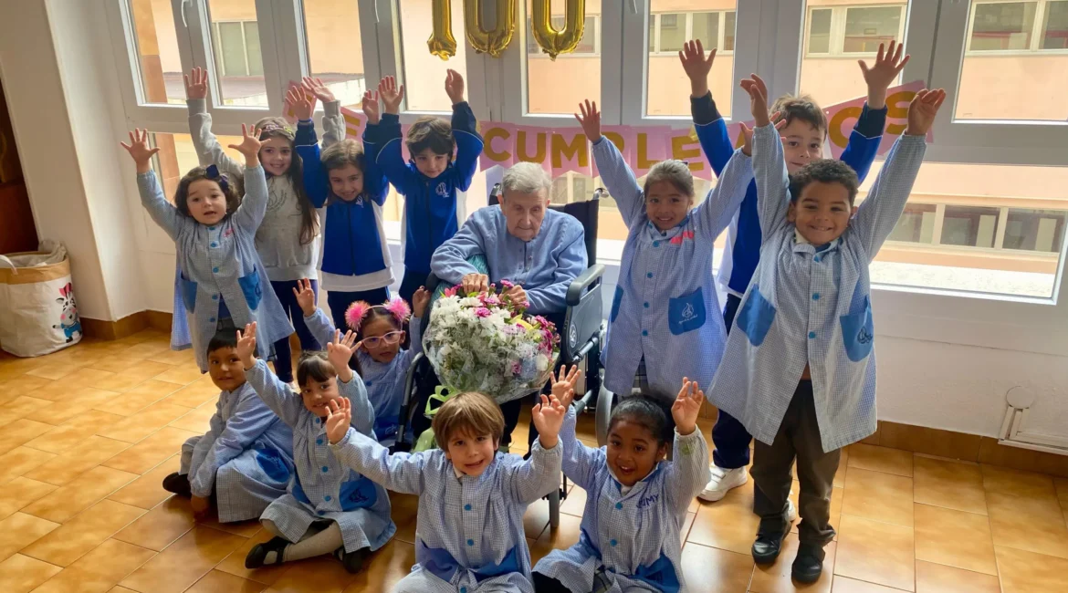Alumnado de Infantil levantando los brazos junto a sor Enriqueta en su 100.º cumpleaños